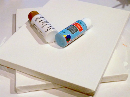 Two white canvases with bottles of white acrylic paint and blue acrylic paint