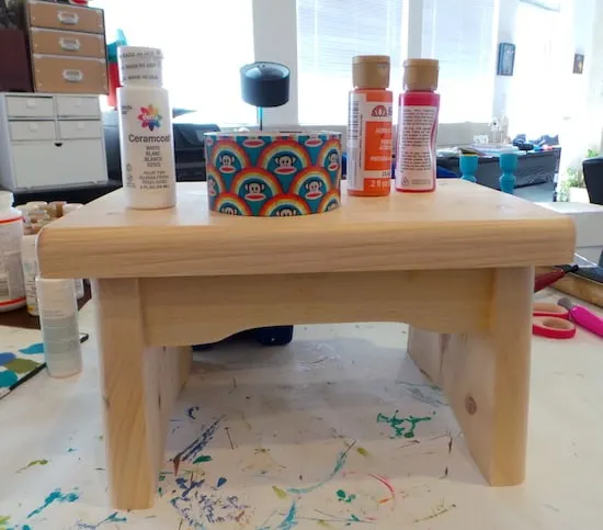 Wooden stool with duct tape and paint bottles sitting on top