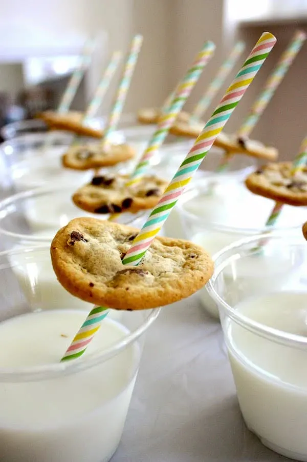 Straws poked through chocolate chip cookies in glasses of milk