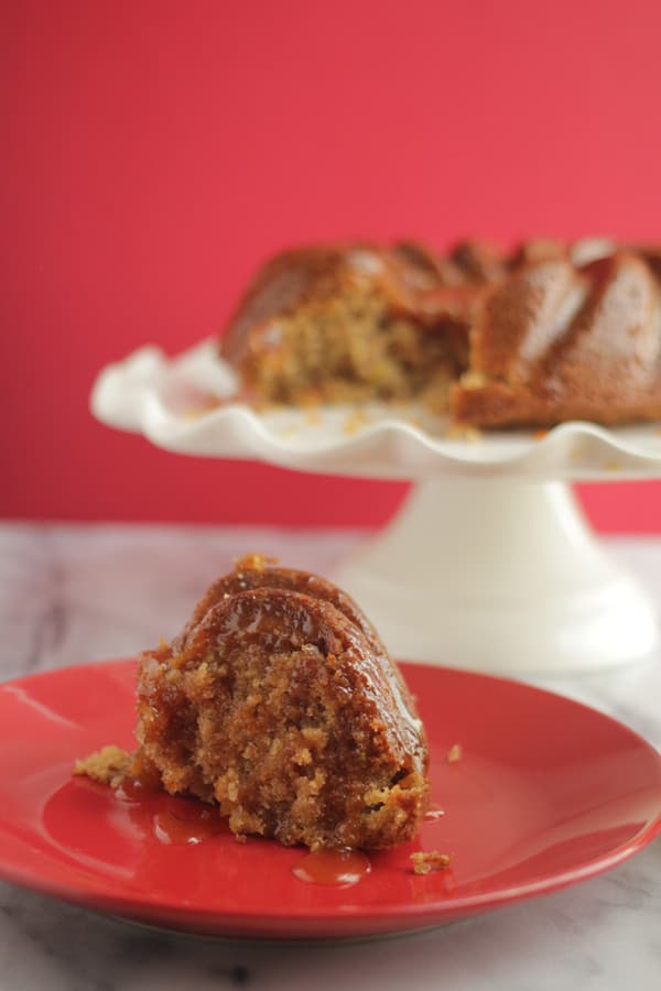 Apple spice cake piece on a plate with the rest of the cake in the background