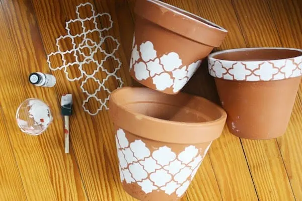 Stenciled clay pots, a used stencil, white paint, and a foam brush with paint on it