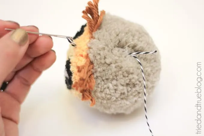 Baker's twine being threaded through the pom pom