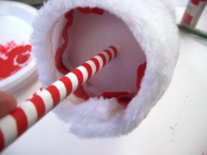 Sticking a dowel rod into the bottom of a foam cone with a Santa hat