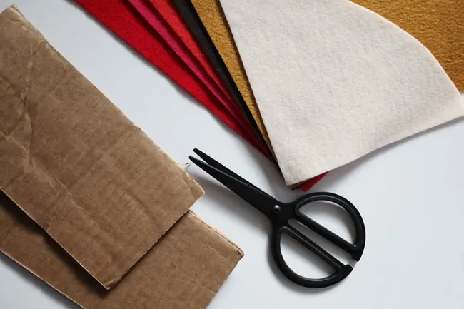 Cardboard, stack of felt in various colors, and scissors with black handles