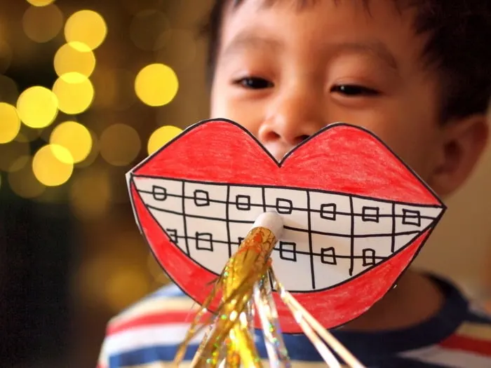 Boy blowing on a DIY photo booth horn that looks like lips and teeth with braces