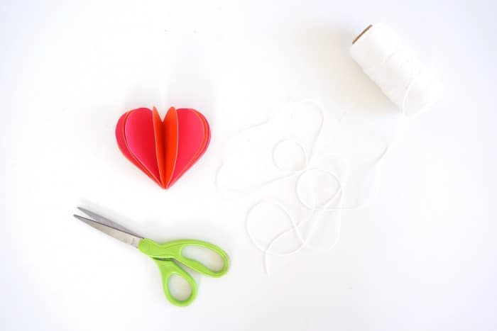 Paper heart with white twine and scissors laying next to it