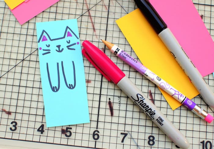 Draw a cat face on a paint chip with pink and black Sharpies