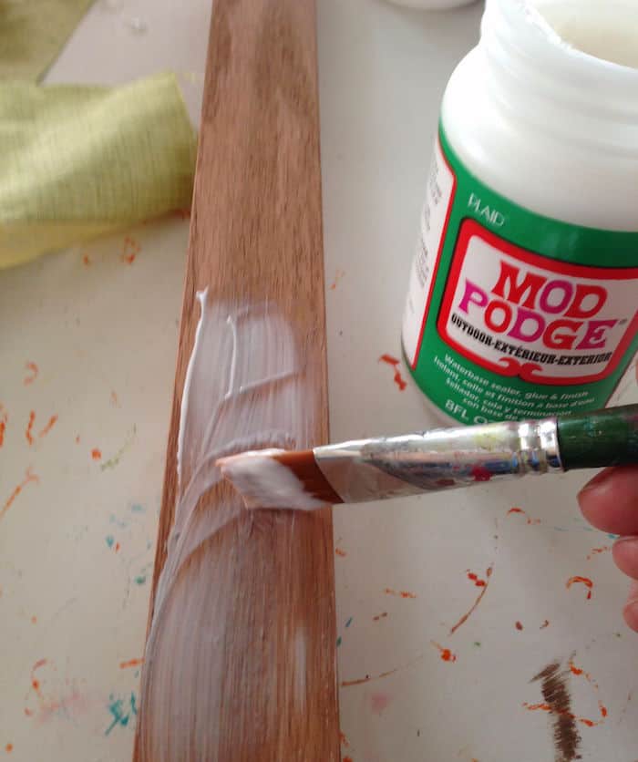Adding Mod Podge to a wood slat with a paintbrush