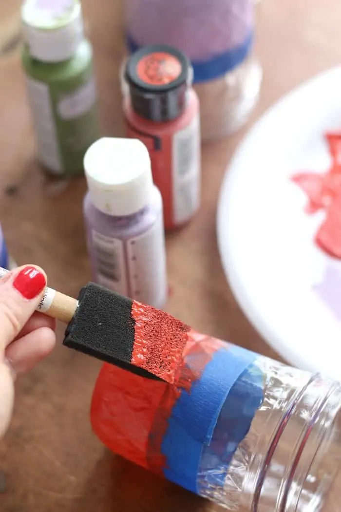 Painting a mason jar with red acrylic paint and a foam brush