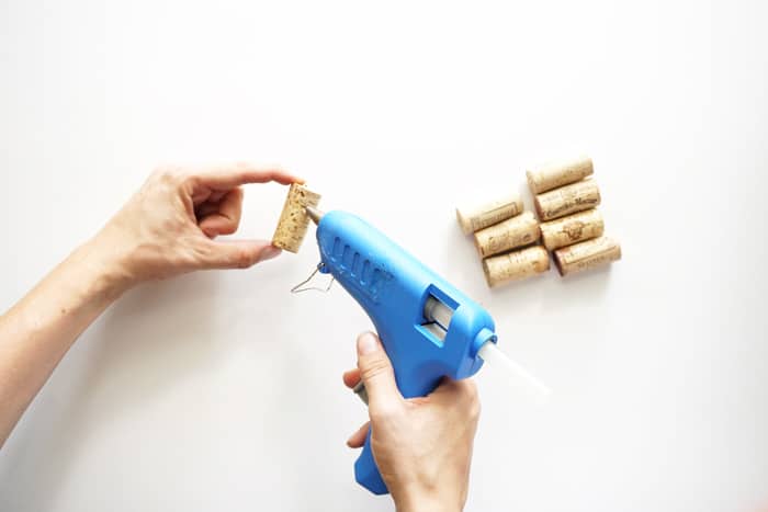 Placing a bead of hot glue down a cork with a hot glue gun