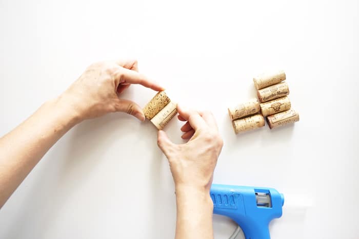 Two hands pressing two corks together with hot glue