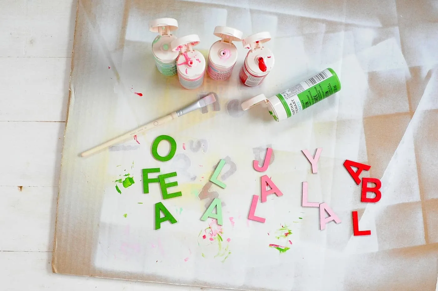 Wood letters painted in green, pink, and red laying on a work surface