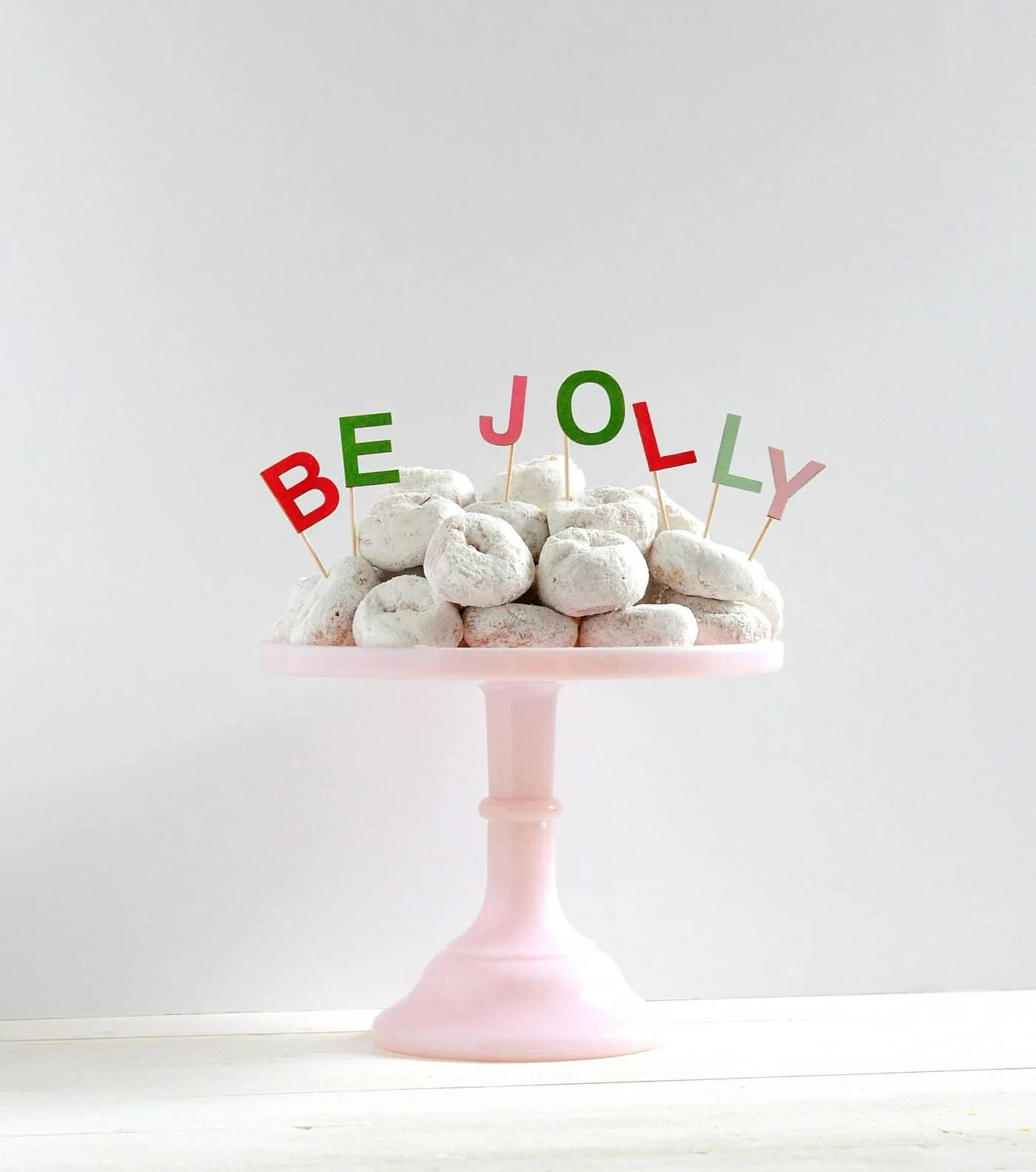 Be Jolly Christmas cake toppers in white powdered donuts on a pink plate