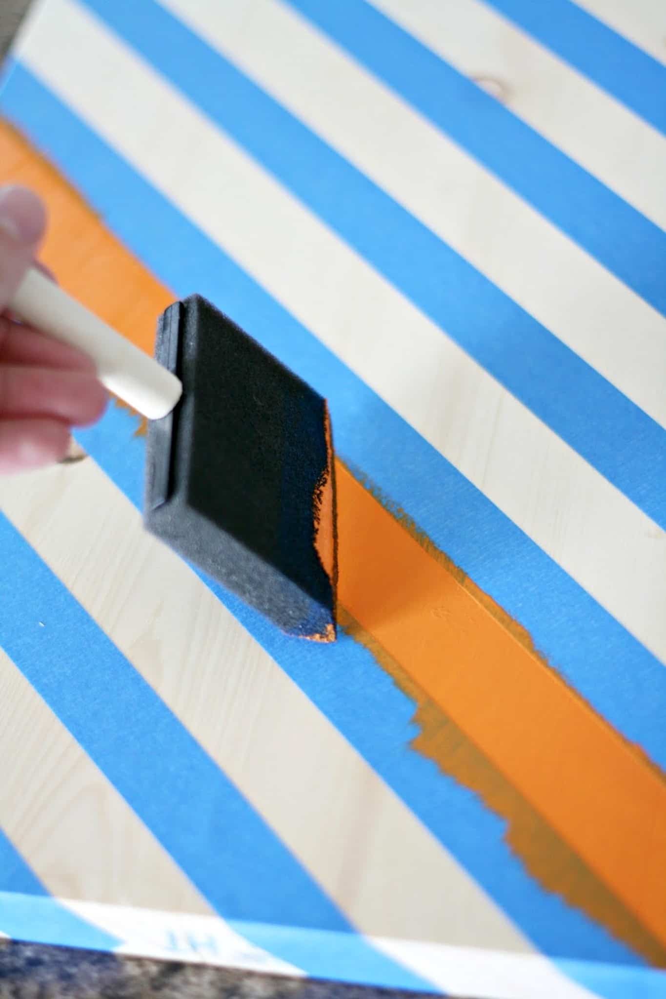 Using a paintbrush to apply orange paint between two lines of painter's tape