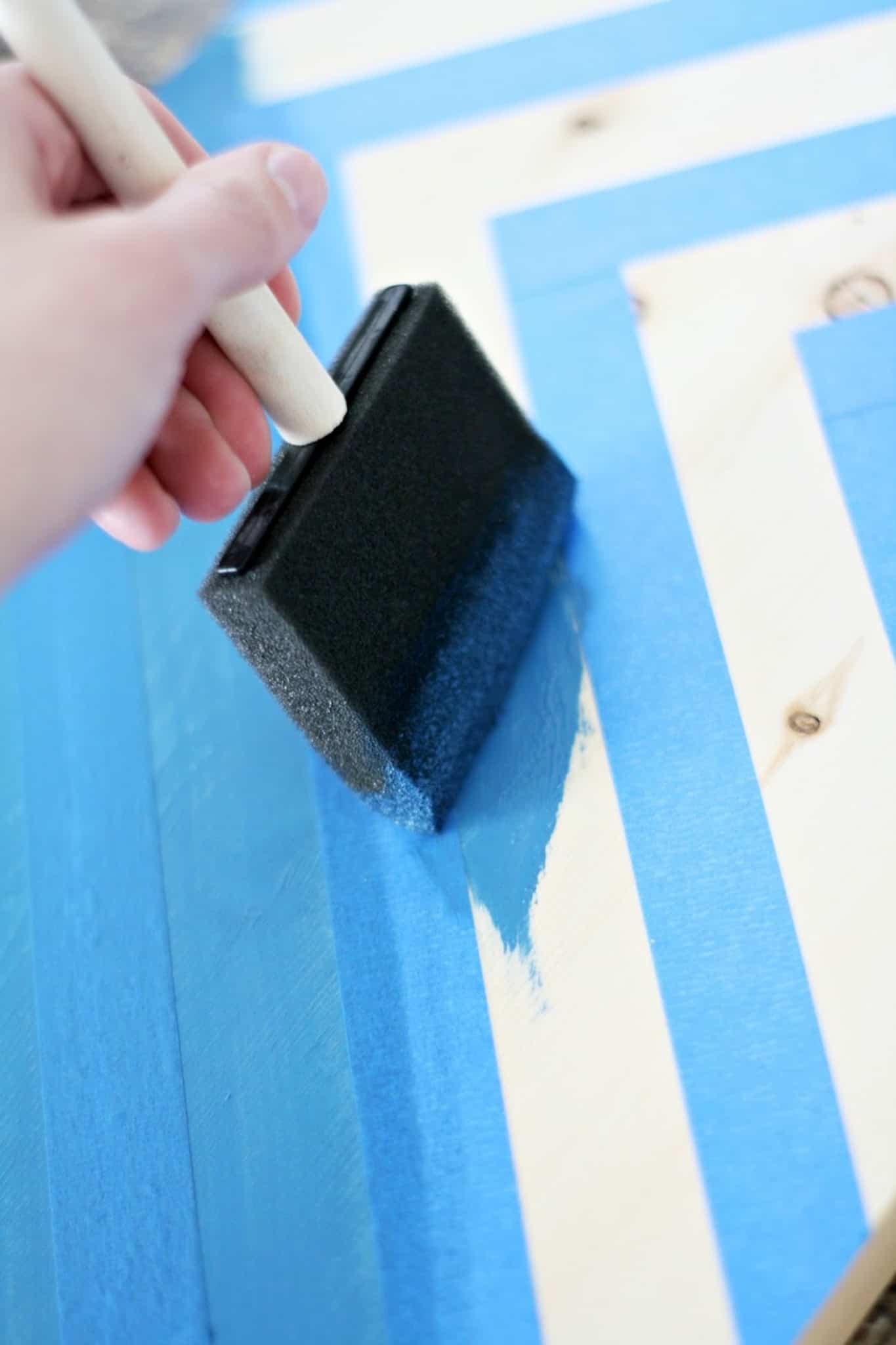 Using a paintbrush to apply blue paint between two lines of painter's tape