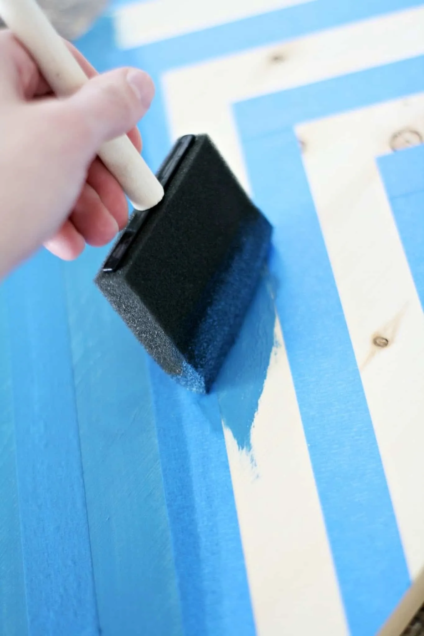 Using a paintbrush to apply blue paint between two lines of painter's tape