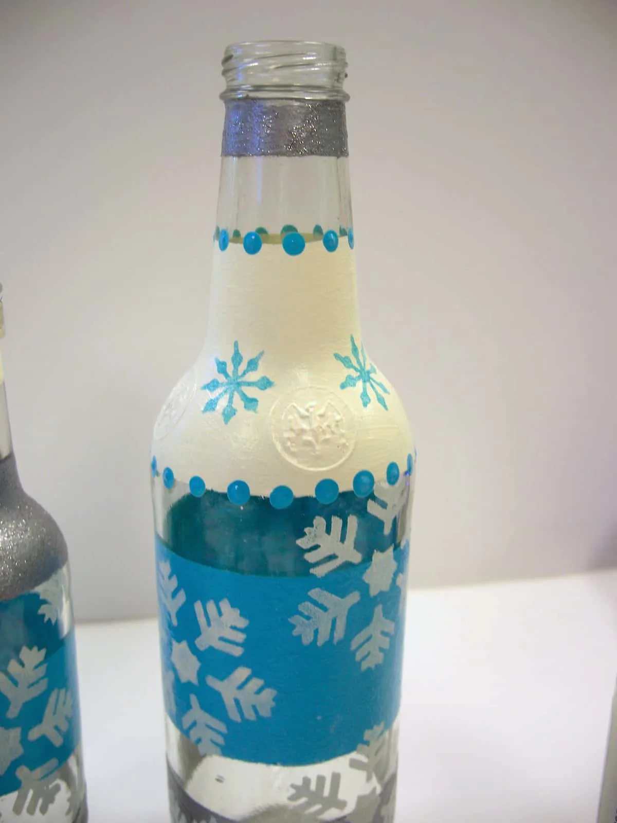 Clear glass bottle painted with cream and silver stripes and blue polka dots