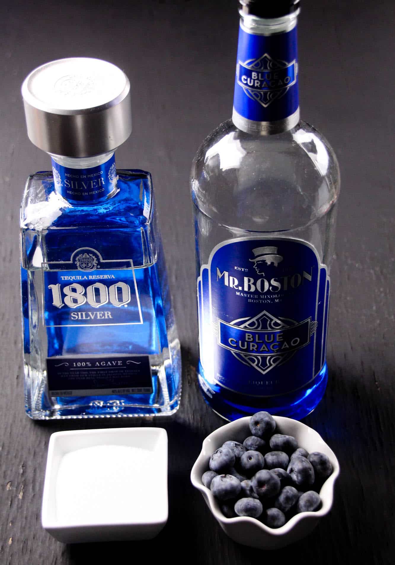 1800 silver tequila, Mr. Boston blue curacao, sugar, and blueberries