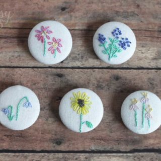 Hand embroidered magnets sitting on a wood board