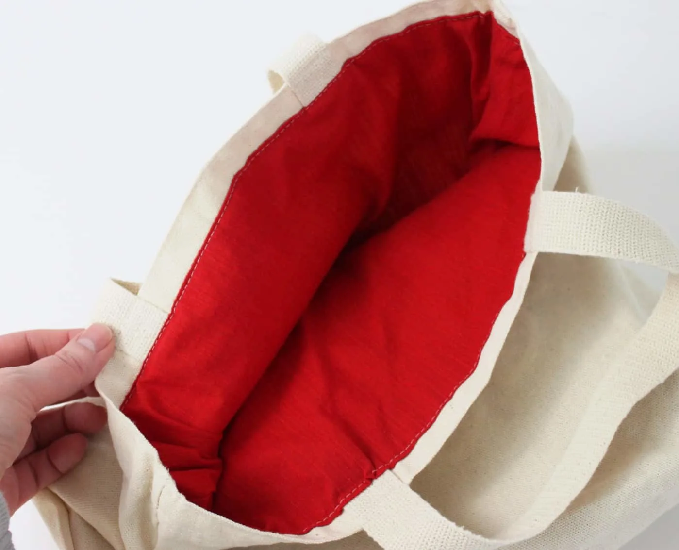 Hand showing the red lining on the inside of the canvas tote