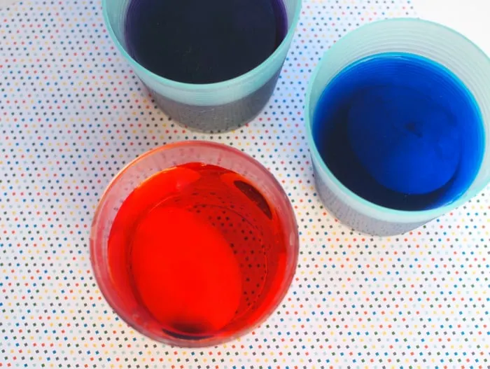 Cracked eggs in food coloring and water in cups