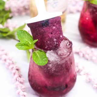 Blueberry alcoholic popsicle in a glass of blueberry simple syrup, wine, and kinky blue