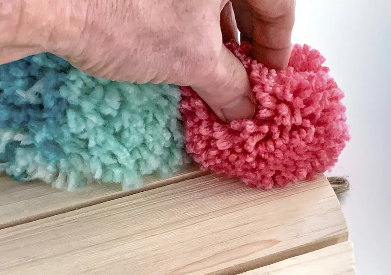 Hand pressing a pom pom down on a wood surface