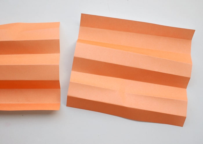 Two sheets of orange origami paper unfolded on a work surface