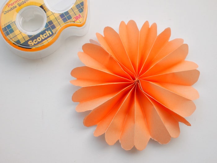 Roll of double stick tape and a paper flower laying on a work surface