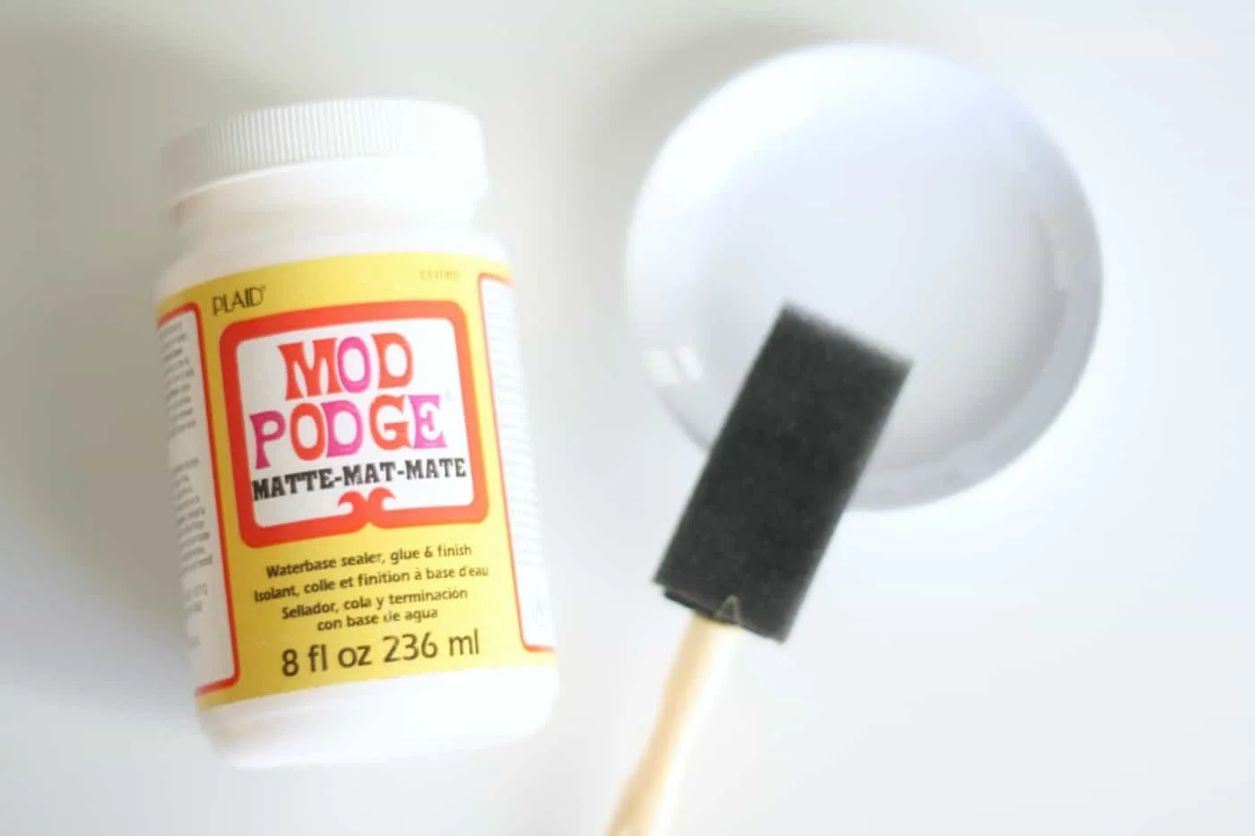 Bottle of Mod Podge Matte, small ceramic white dish, and a foam brush
