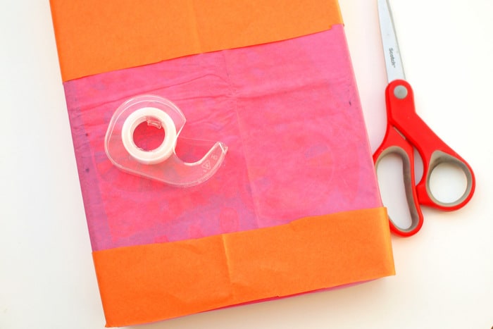 Gift wrapped in pink tissue paper and additional orange paper with a pair of scissors and tape