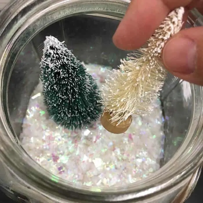 Placing bottle brush trees into a glass jar filled with artificial snow