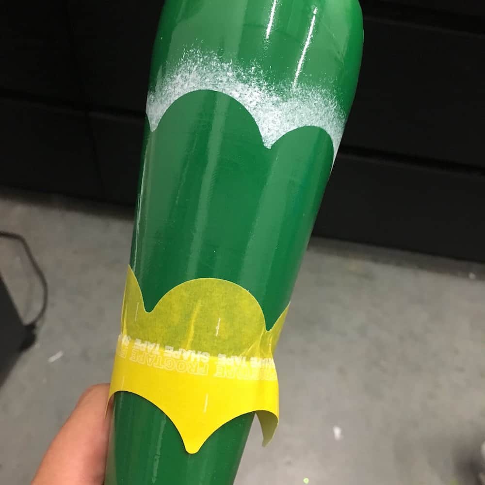 A green spray painted bottle with white snow effect and scalloped stencil tape