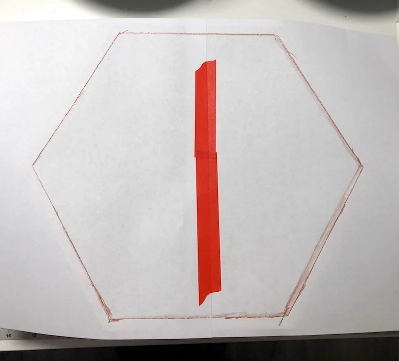 Two pieces of paper taped together with washi tape with a hexagon shape drawn on with red pencil