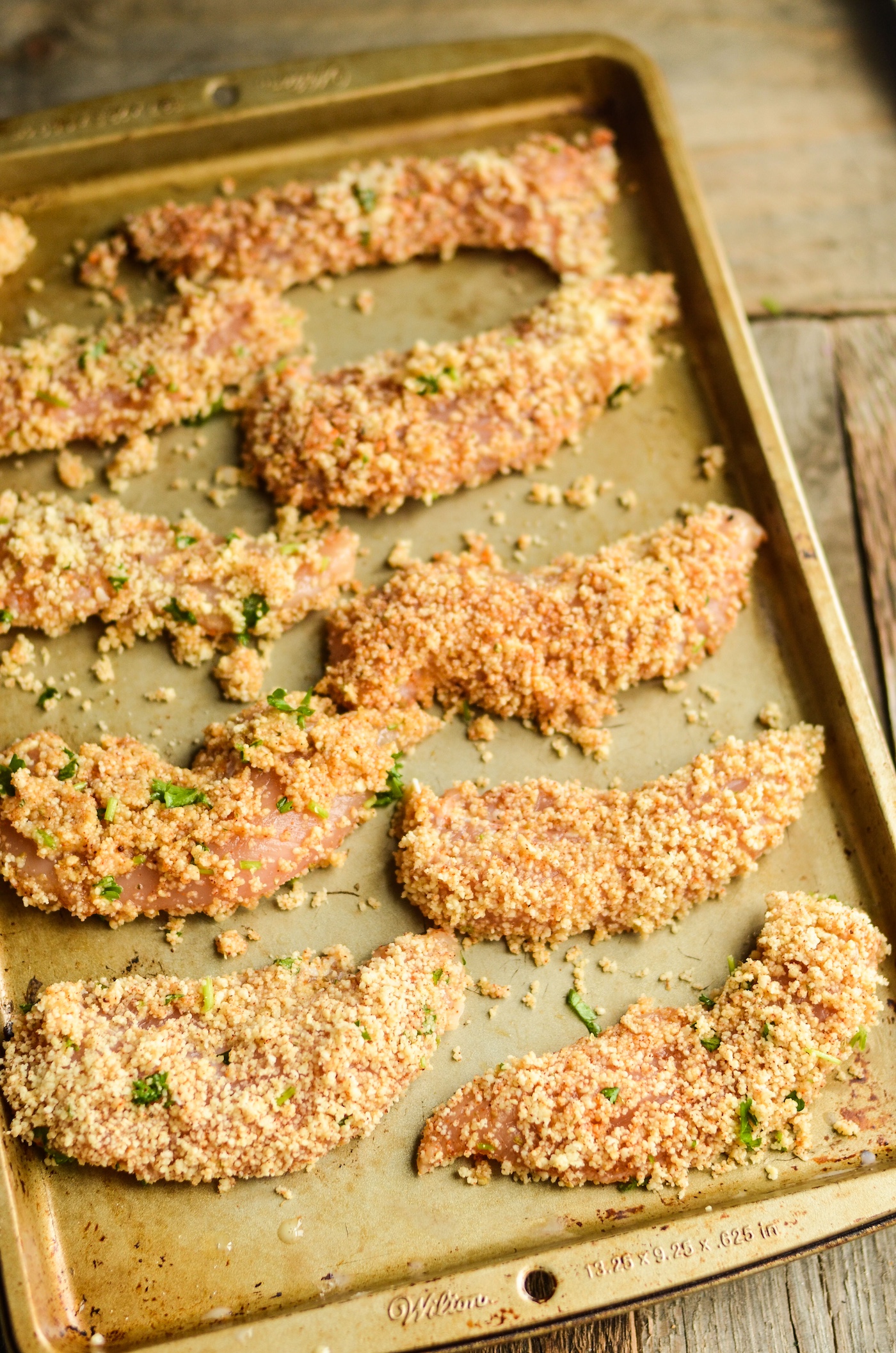 Chicken tenders coated in almond flour on a baking sheet