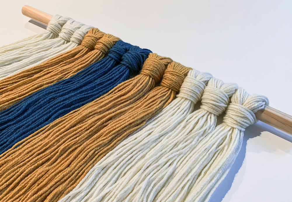teal mustard and white yarn attached to a dowel rod
