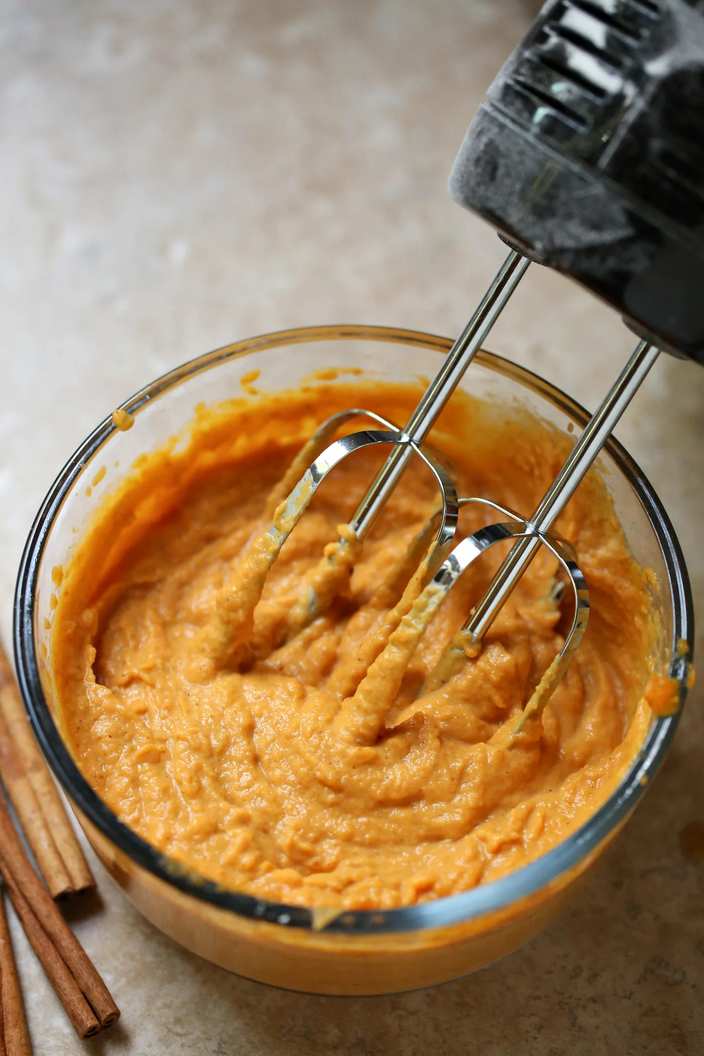 Mixing pumpkin puree, heavy cream, and pumpkin pie spice in a bowl with a hand mixer