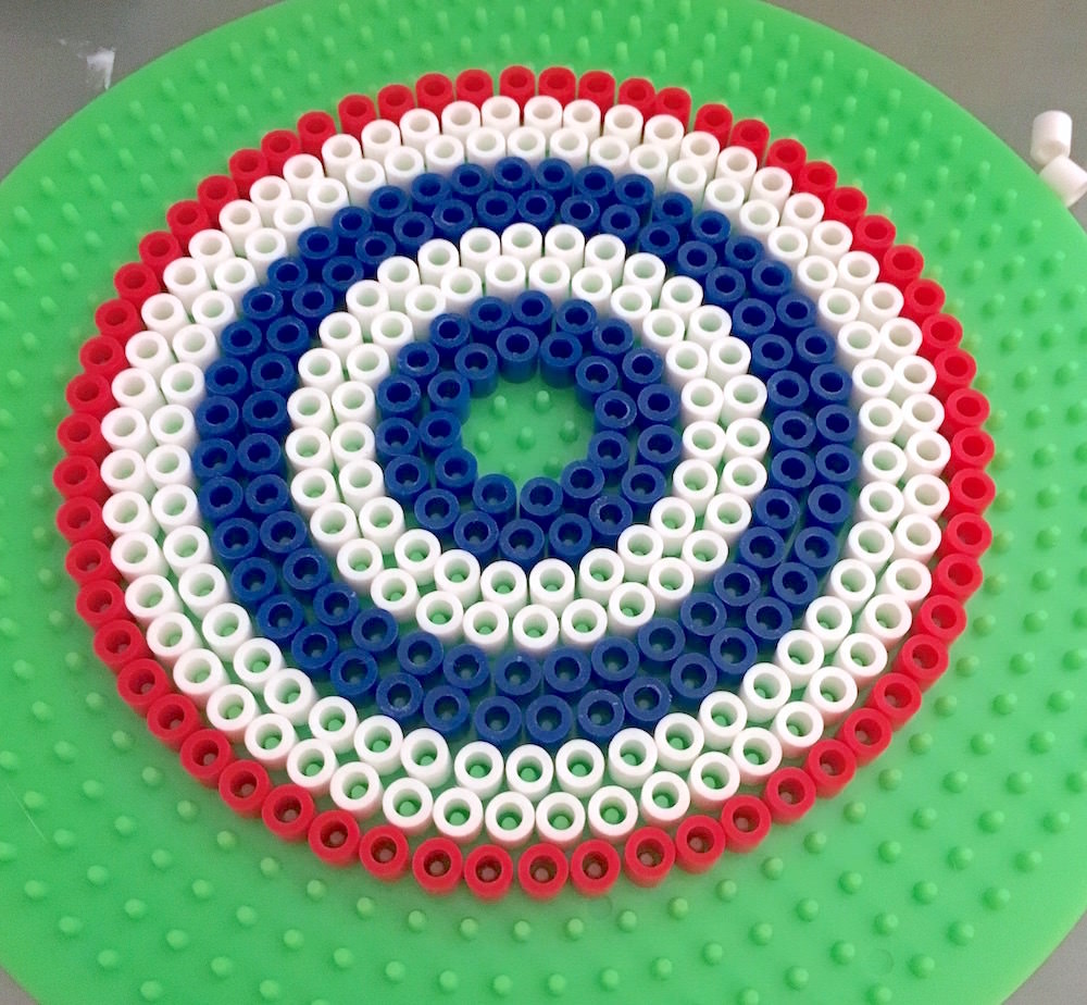 Perler bead drink cover laid out on a pegboard