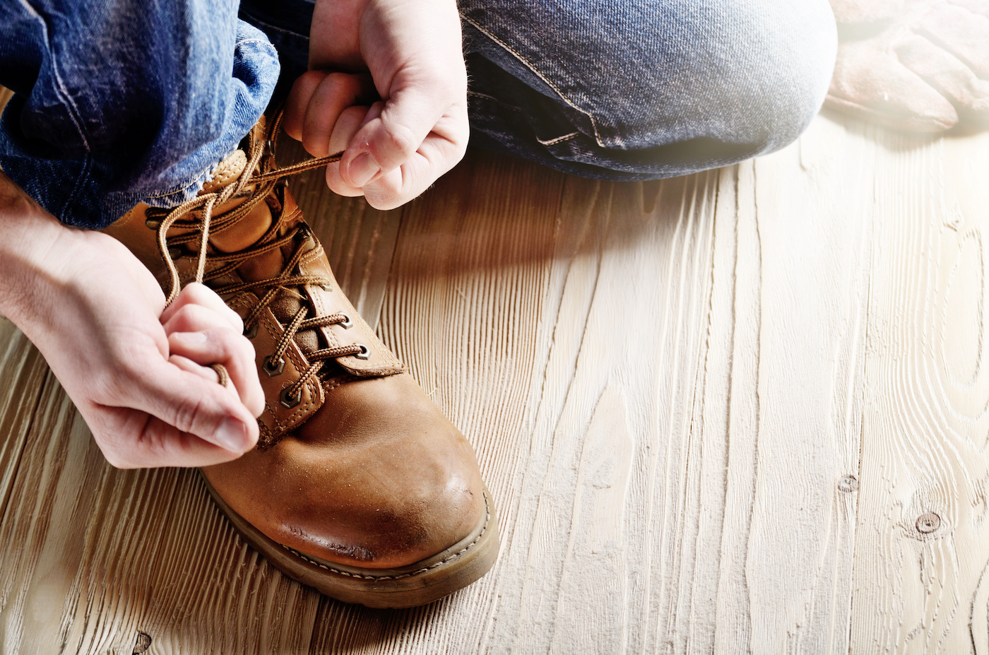 Carpenter in blue jeans tying shoelaces of yellow work boots on on wooden floor