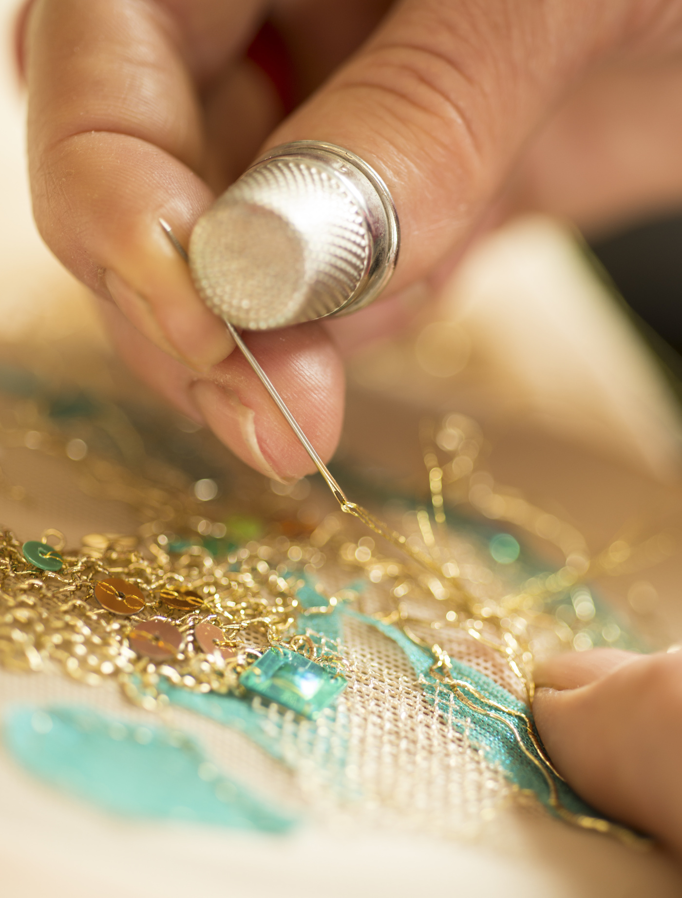 Hands and thimble doing embroidery with gold thread