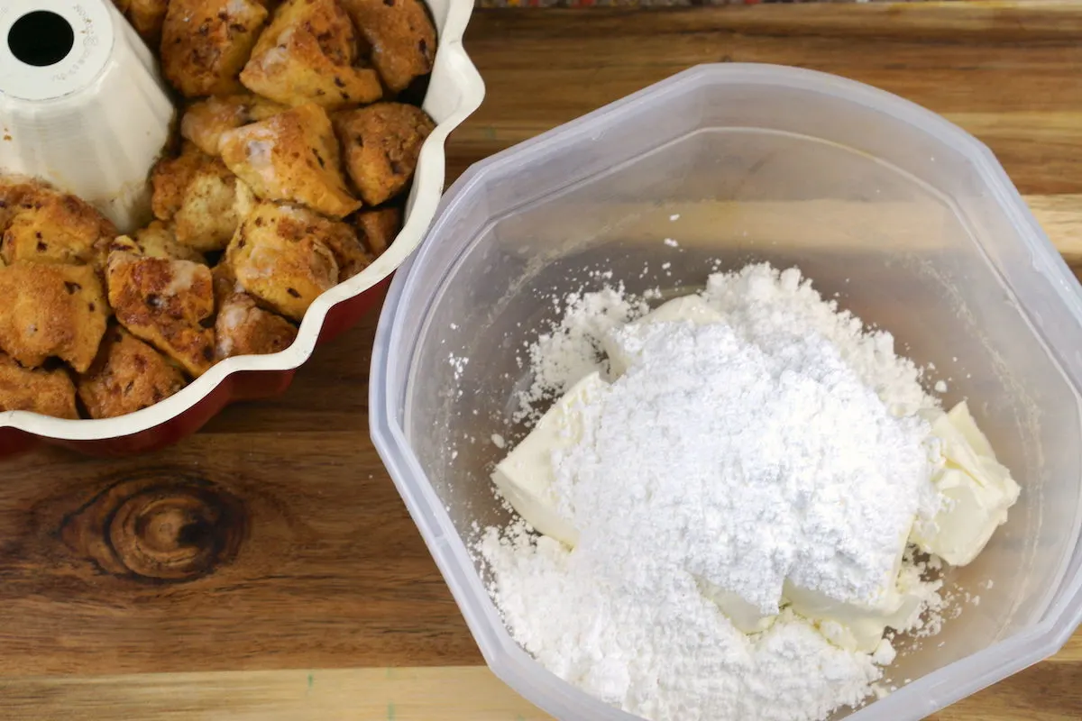 Baked pumpkin monkey bread next to a container filled with butter and powdered sugar