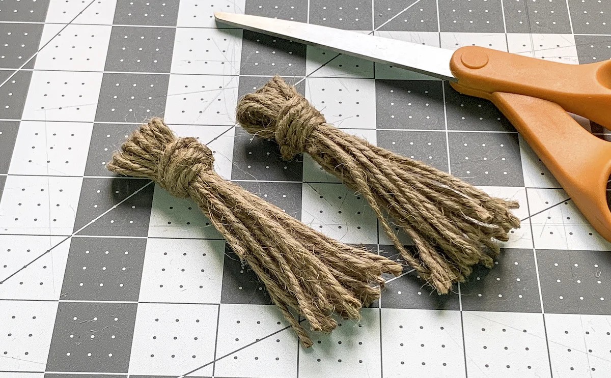Two twine tassels laying on a craft mat with a pair of scissors