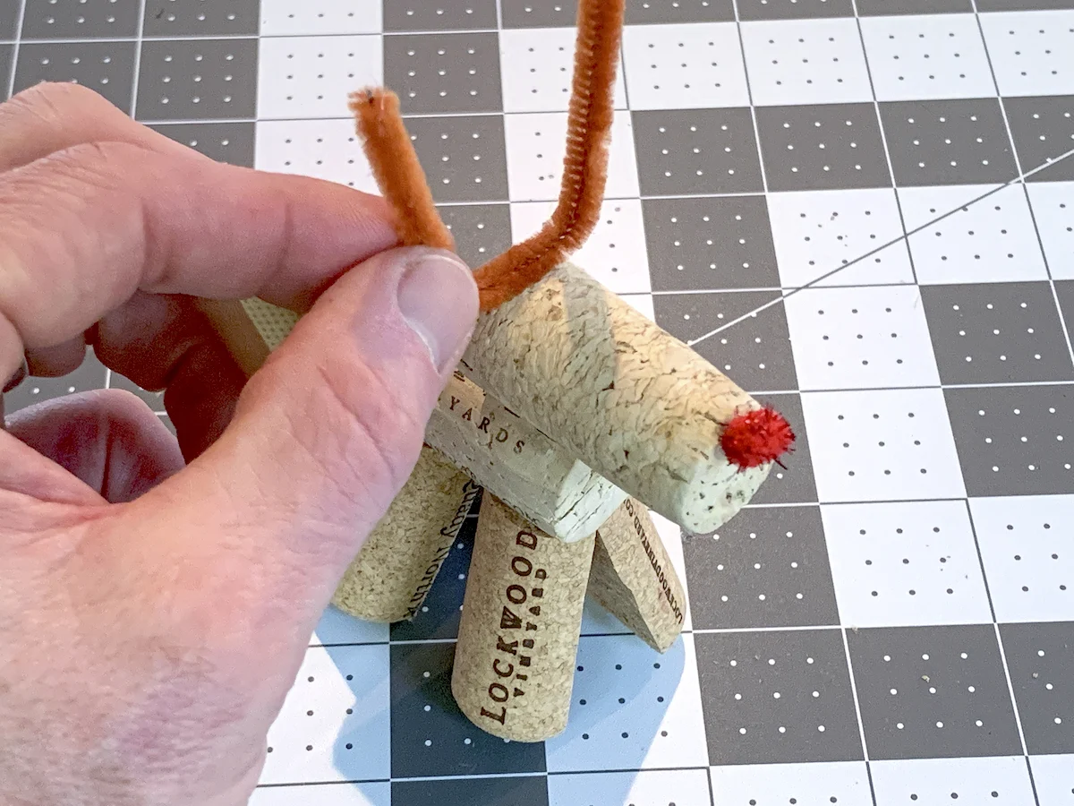 Adding brown pipe cleaners to a wine cork reindeer as antlers