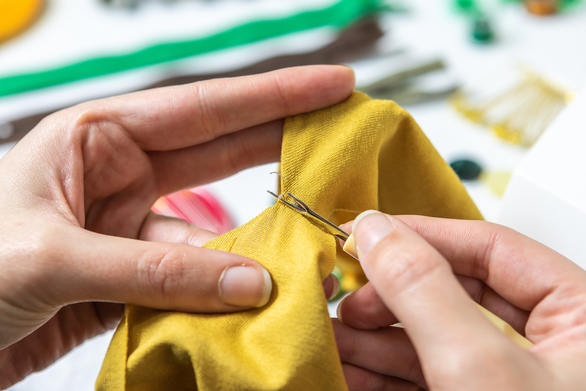 Hand-using-a-seam-ripper-on-gold-fabric