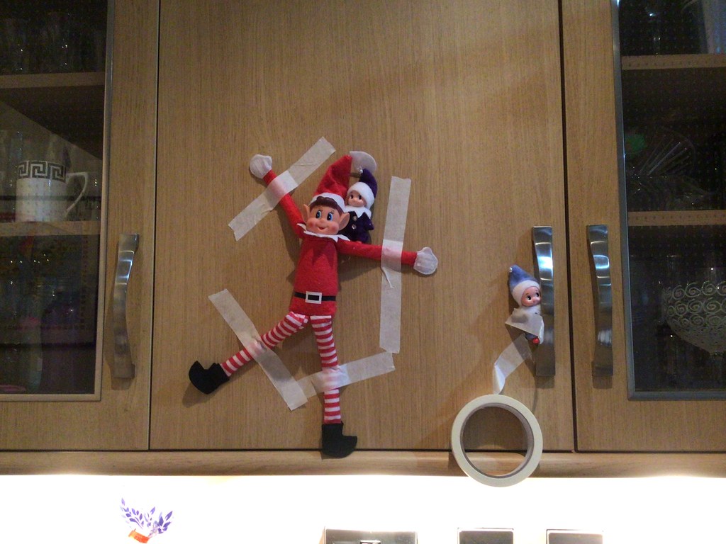 Elf on the shelf stuck to a cabinet with tape