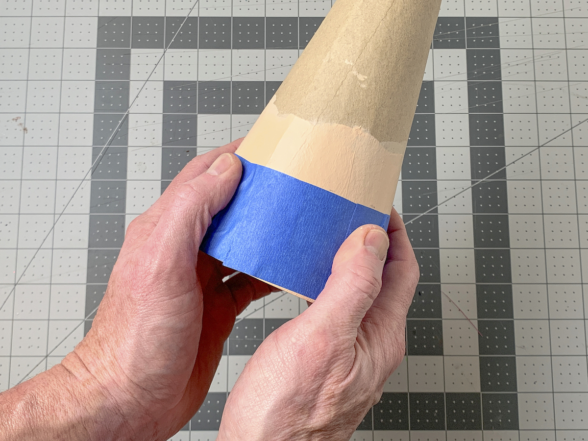 Hand wrapping painter's tape around the base of a paper mache cone