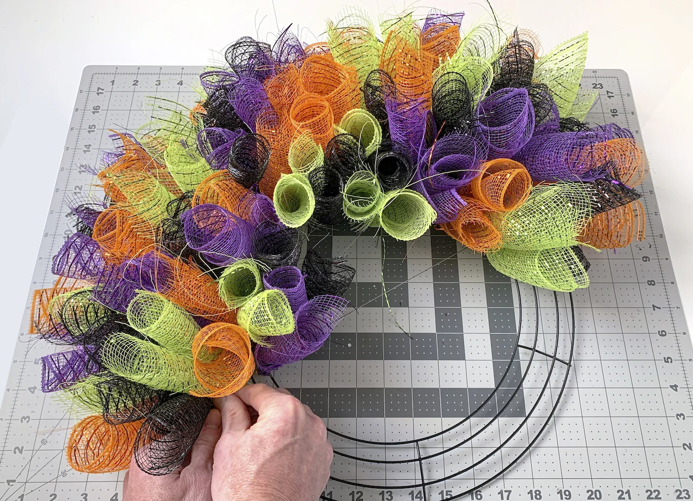 halloween deco mesh being adding to a wreath form with pipe cleaners