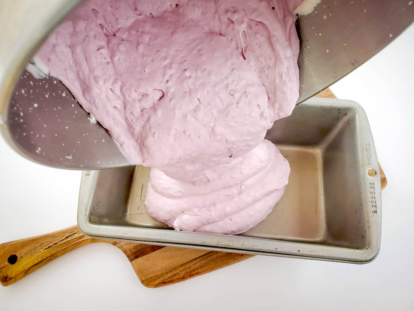 Pouring no churn raspberry ice cream into a chilled bread pan