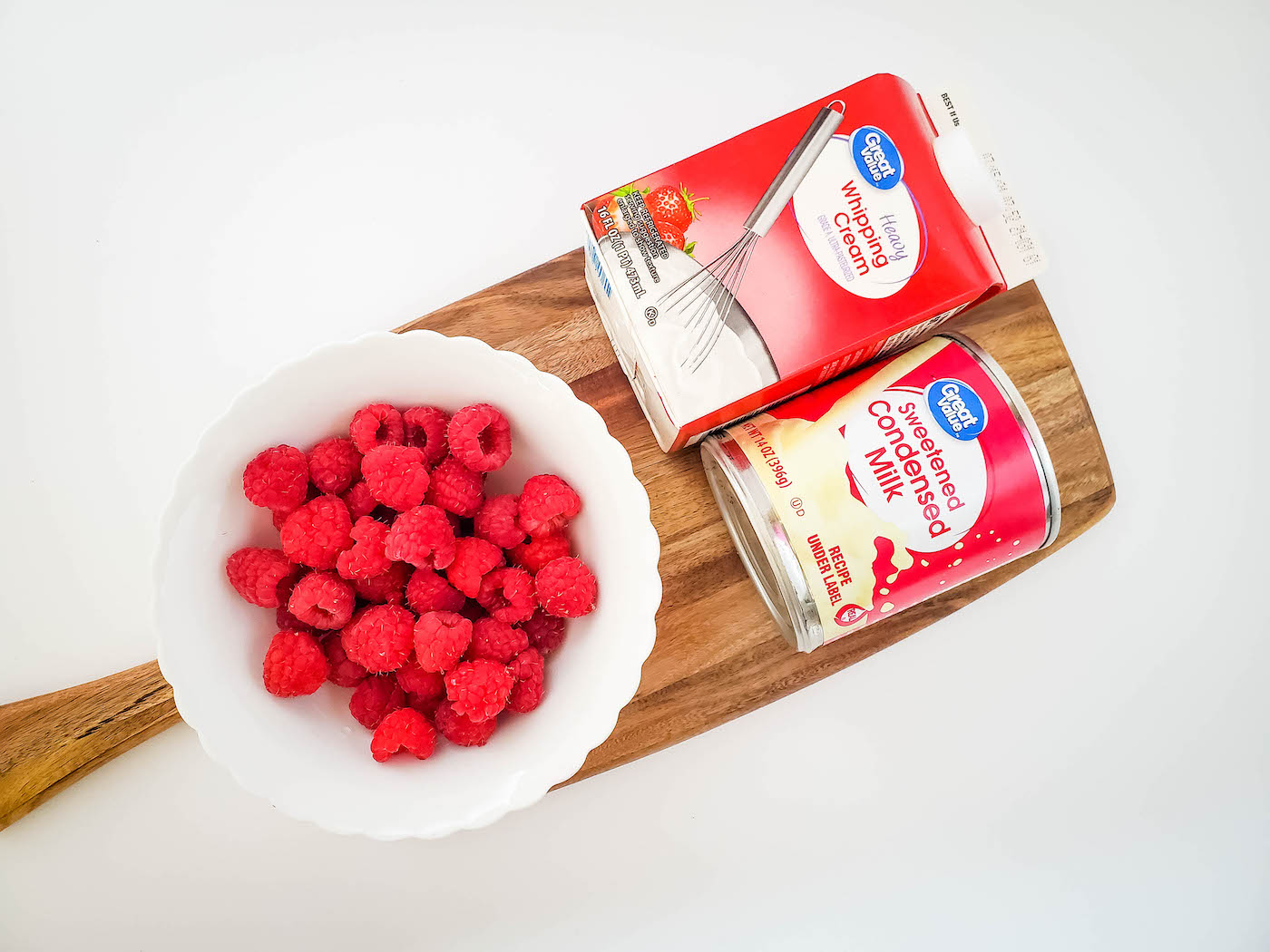 heavy whipping cream, sweetened condensed milk, and raspberries in a bowl on a breadboard