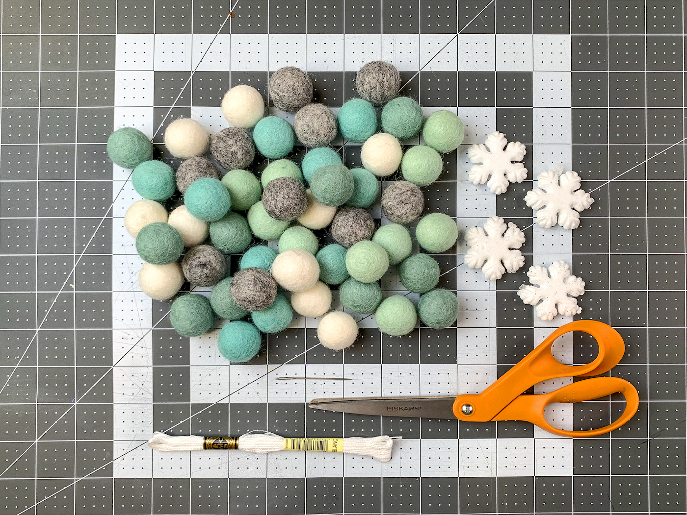 Felt balls, foam snowflakes, embroidery floss, scissors, and a tapestry needle